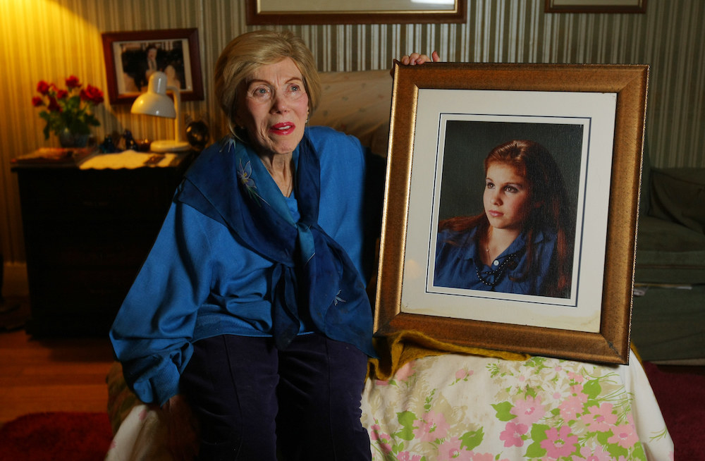 a woman sitting next to a large portrait of her younger self