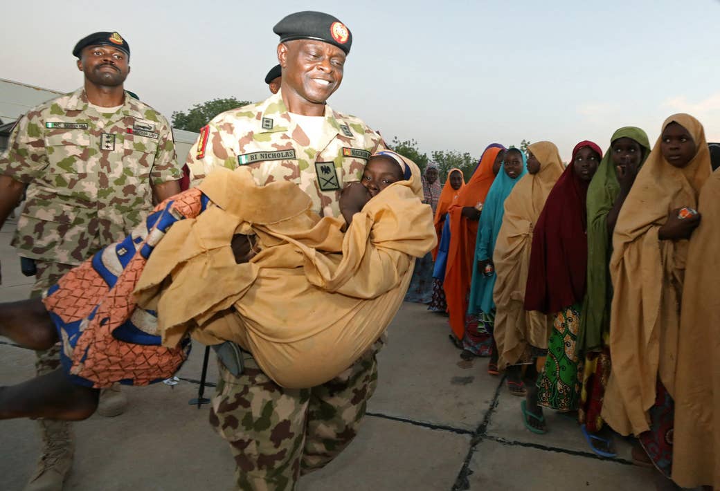 Major General Rogers Nicholas carries one of the newly released Dapchi schoolgirls as others wait to board a plane at the air force base in Maiduguri, Nigeria.