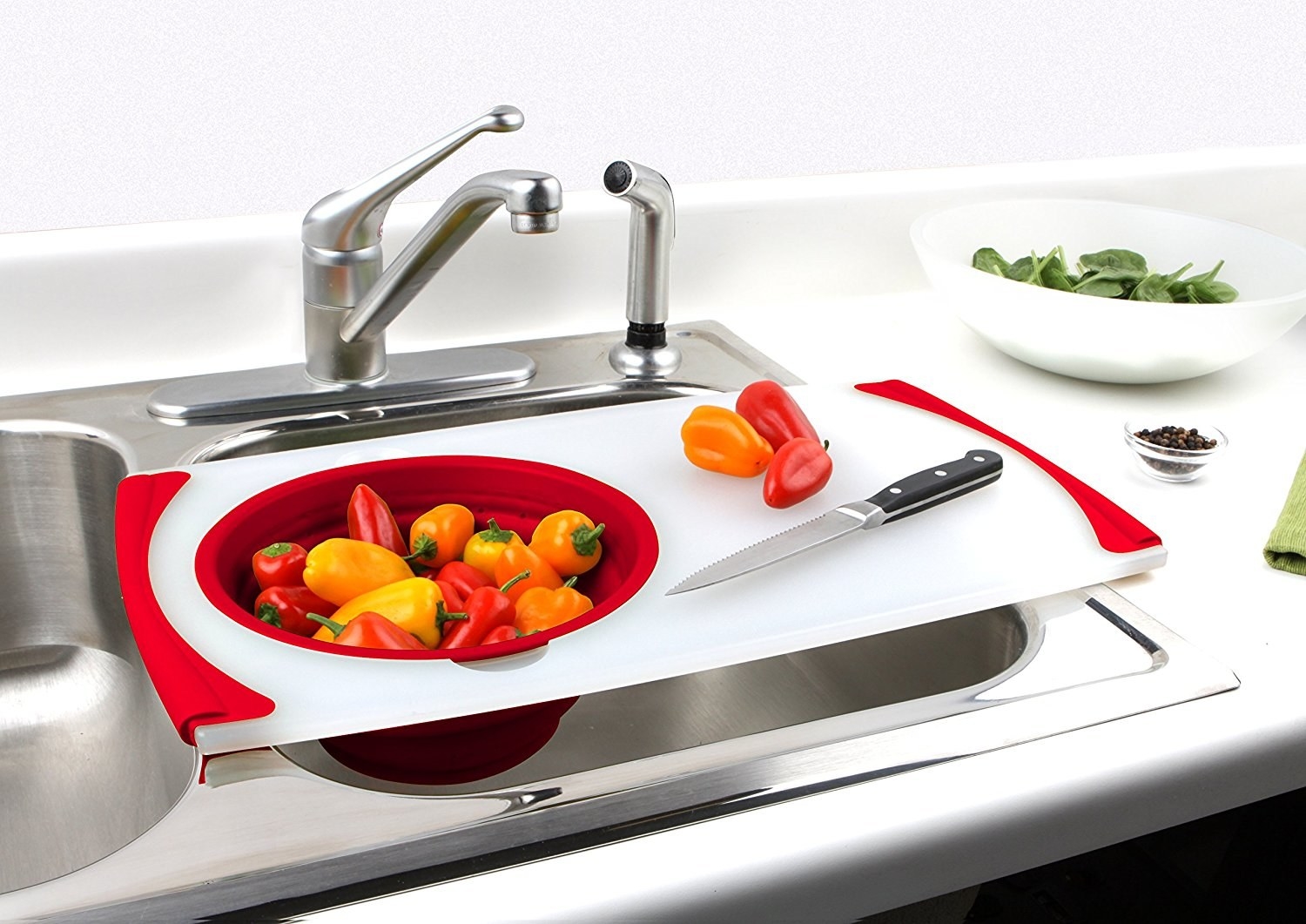a white cutting board with red accents and a strainer set on one side of it to place over the sink for drainage