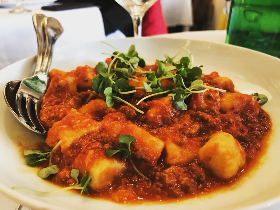 The doughy, chewy gnocchi is mixed in with rich ragu sauce with microgreens on top.