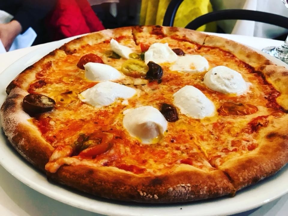 The signatrure Milana Pizza is topped with tomato and cherry tomatoes on thin crust dough with cantal cheese and a scoop of creamy burrata on each slice.