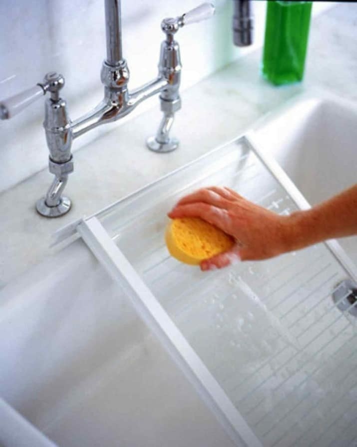 person washing fridge shelf in a sink with a sponge
