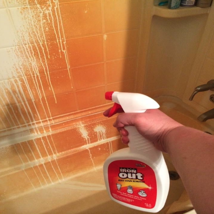 reviewer's hand spraying product on shower wall that's completely orange with rust; where the product has been sprayed, the rust has disappeared 