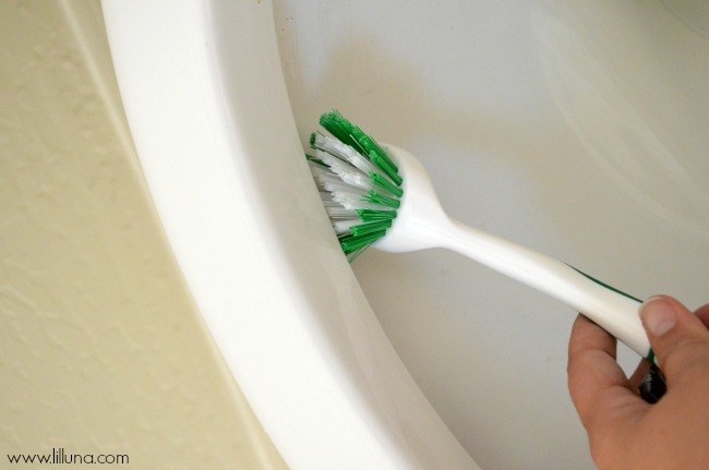 hand using scrub brush under rim of toilet