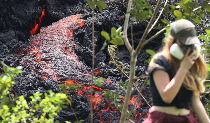 Lava flows at a new fissure on May 12 as a local resident walks nearby after taking photos.