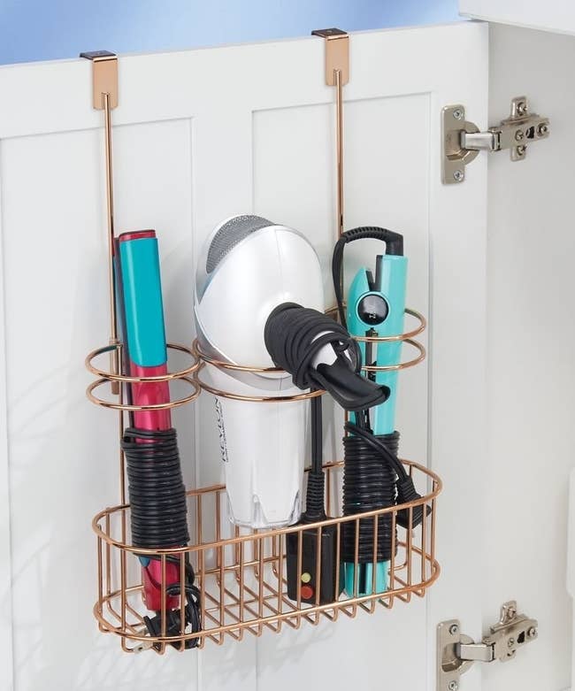 the gold over-the-door organizer with metal circles holding a curling iron, blow dryer, and straightener
