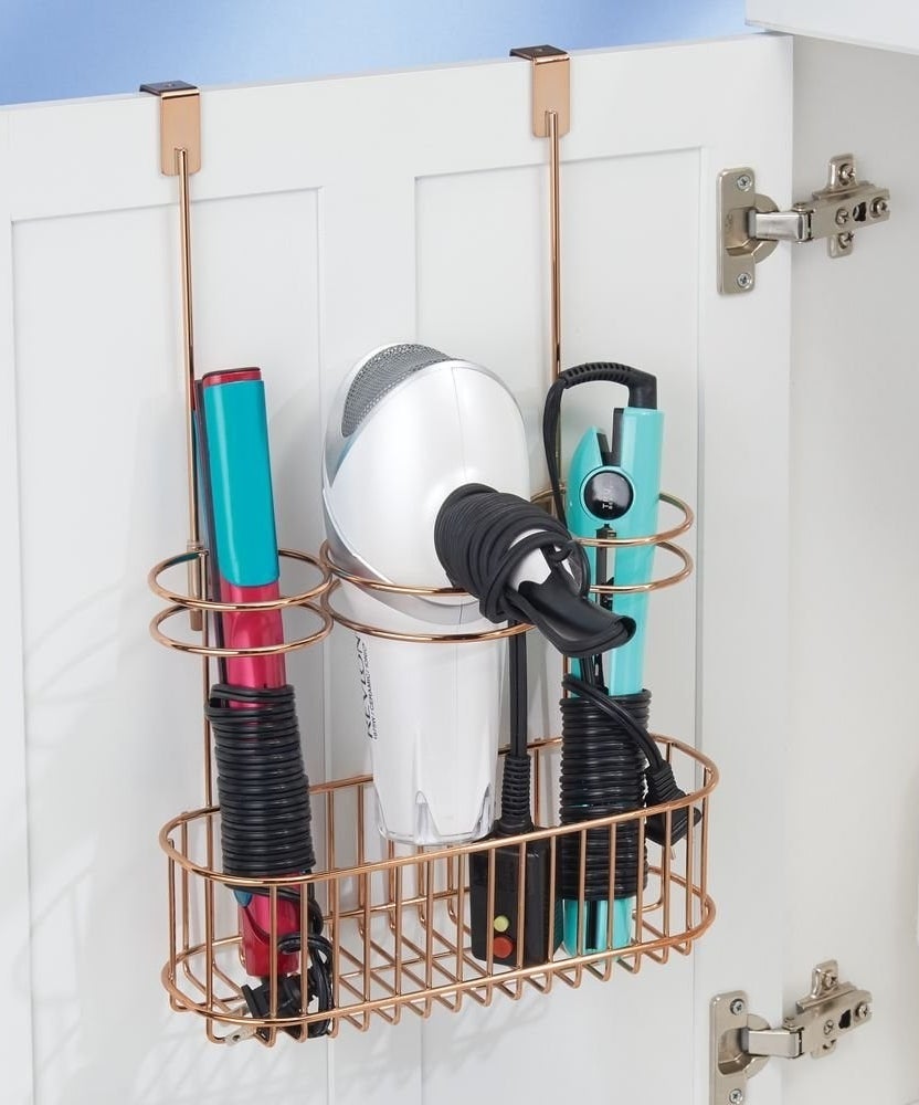 Over cabinet door metal wire holder with three hot tools slid into rings, balanced on wire shelf below