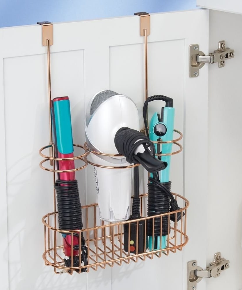 the gold over-the-door organizer with metal circles holding a curling iron, blow dryer, and straightener