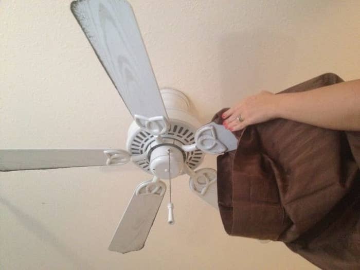 A person uses an old pillow case to remove dust from a ceiling fan blade