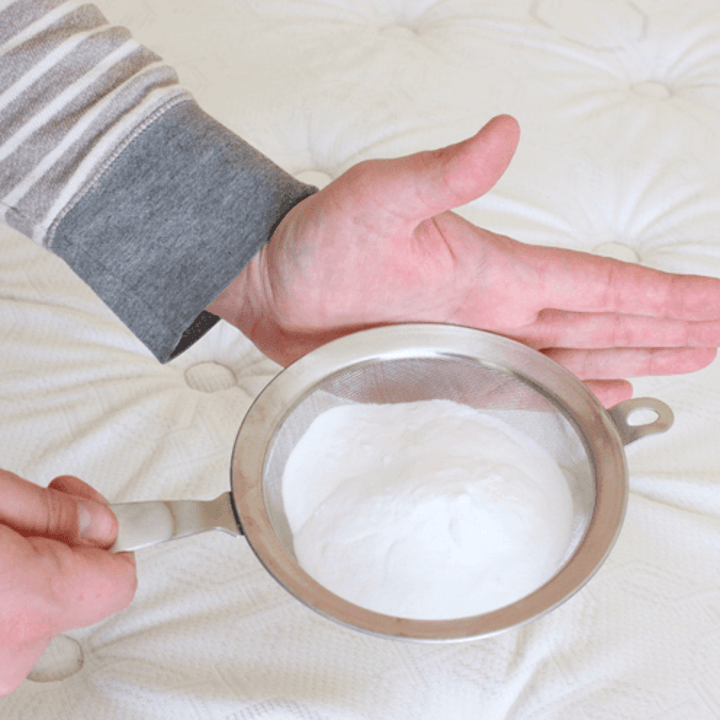 blogger's hands sprinkling baking soda over mattress using kitchen sifter