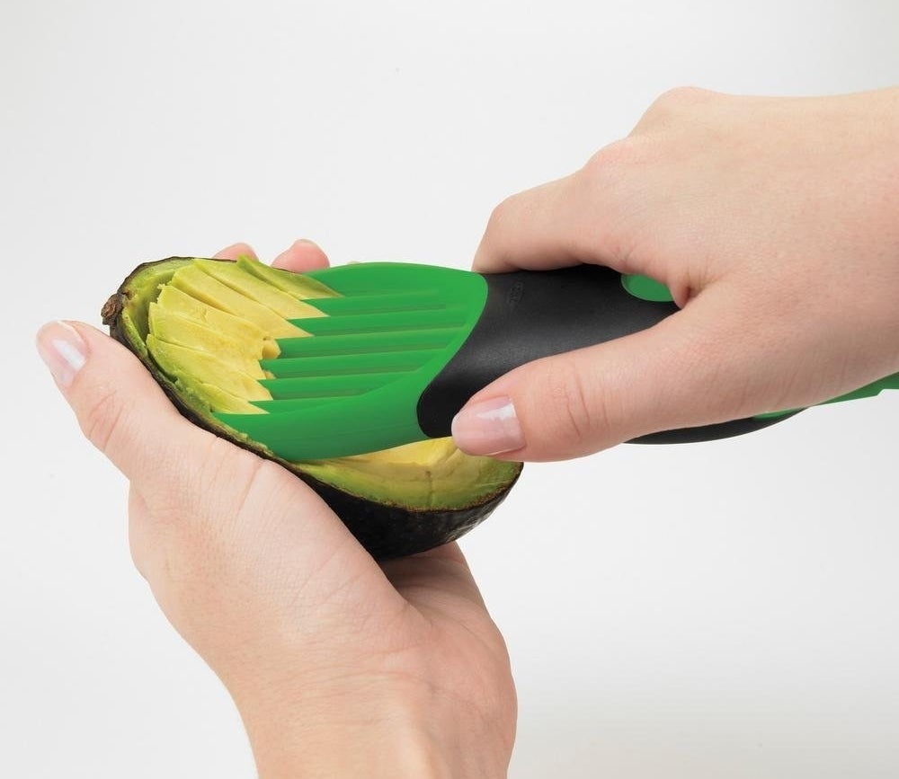 person using the tool to slice open half of an avocado 
