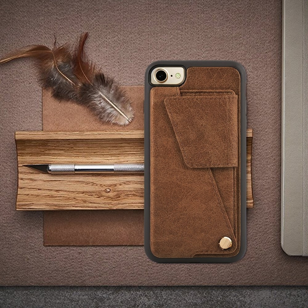 the brown leather card holder photographed on a work desk next to a pen and a feather