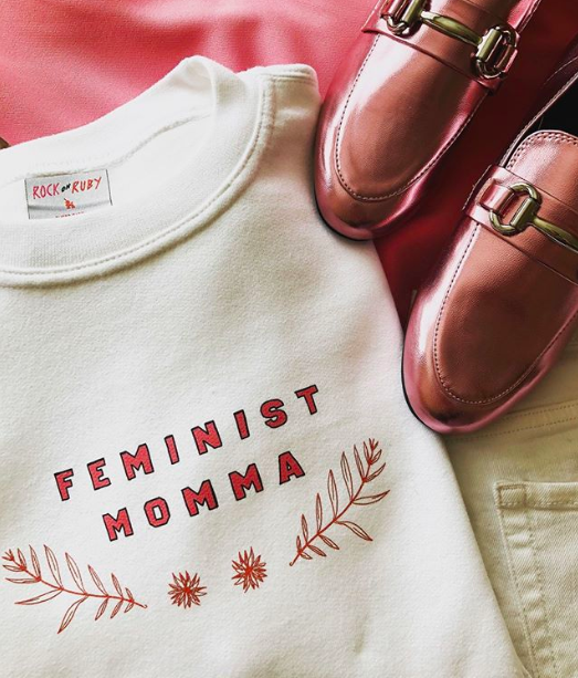 A sweatshirt that says &quot;Feminist momma&quot; next to a pair of shoes.