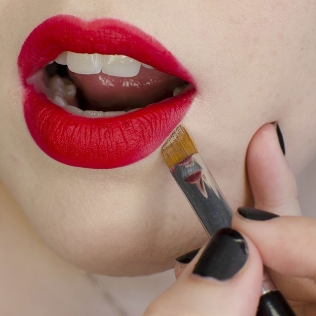 Someone applying the concealer with an angled brush to fix a red lipstick line