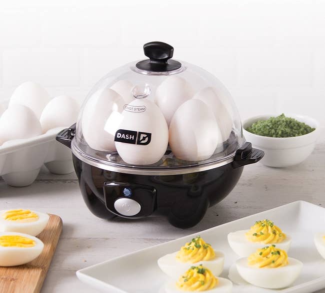 an electric egg cooker filled with eggs next to a plate of deviled eggs