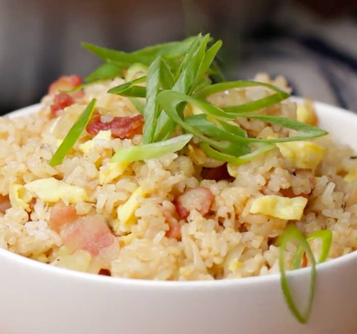 A delicious bowl of fried rice garnished with green onions, featuring bits of bacon and scrambled eggs