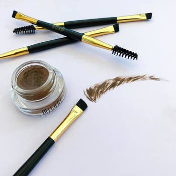 The Milani brow color, which comes in a gel pot, plus the double-sided applicator (one side angled brush, one side spoolie), plus a fake eyebrow drawn on a surface to show what the strokes of the gel color look like