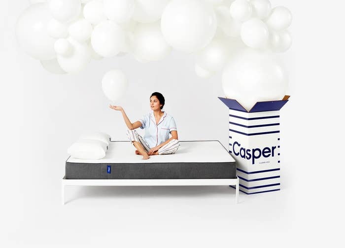 model sits on mattress while white balloons pour out of the casper box