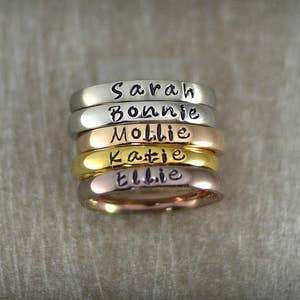 silver, rose gold, and gold stackable rings that say Sarah and other names on front

