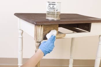 A person applying the chalked paint to a side table
