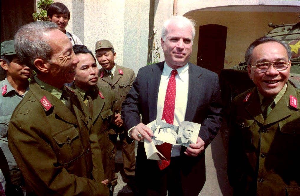 McCain holds up photos of himself outside the Vietnam Military History Museum in Hanoi on Oct. 19, 1992. The photos were delivered by Col. Pham Duc Dai (left), director of the museum, and Col. Tran Bien (right), representative on the MIA issue at the Ministry of Defense, as a gift for visiting the museum.