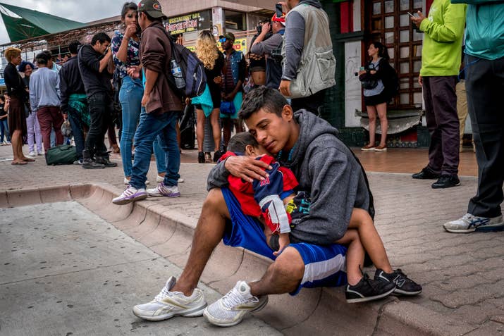An asylum seeker holds his sleeping son as caravan members prepare to turn themselves in to US border officials and formally request asylum.