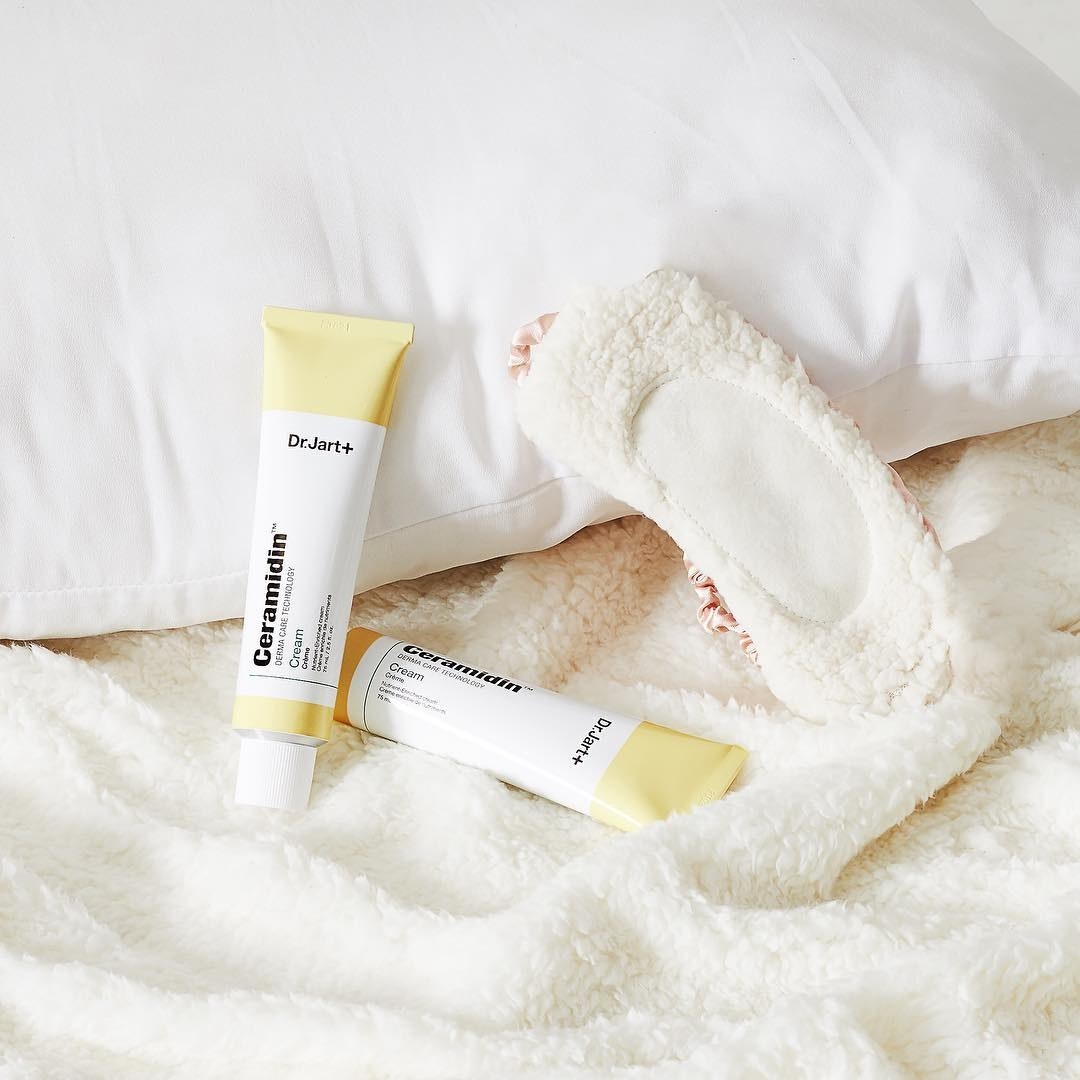 tubes of the cream styled on a blanket and pillow
