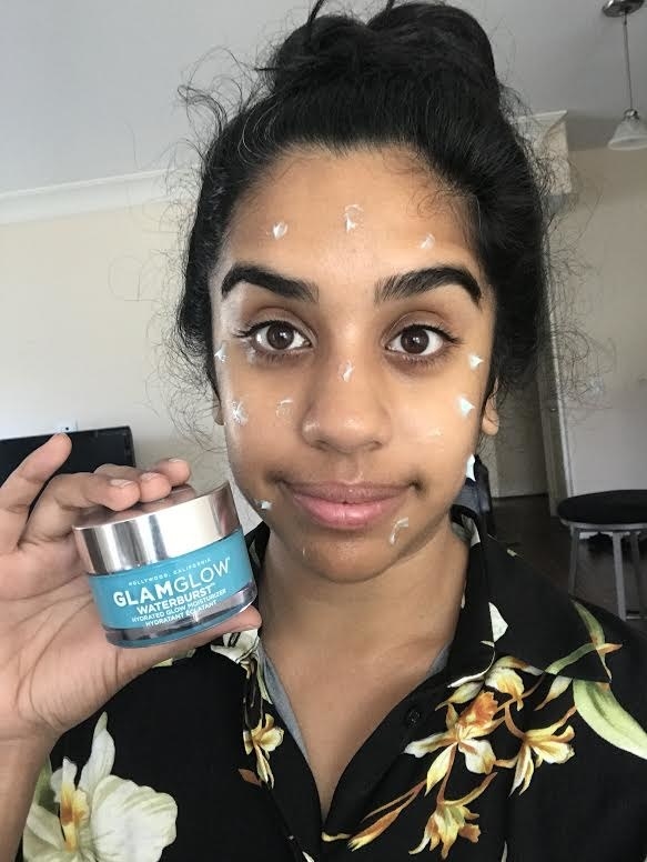 A person holding the ar of lotion with specks of it on their face