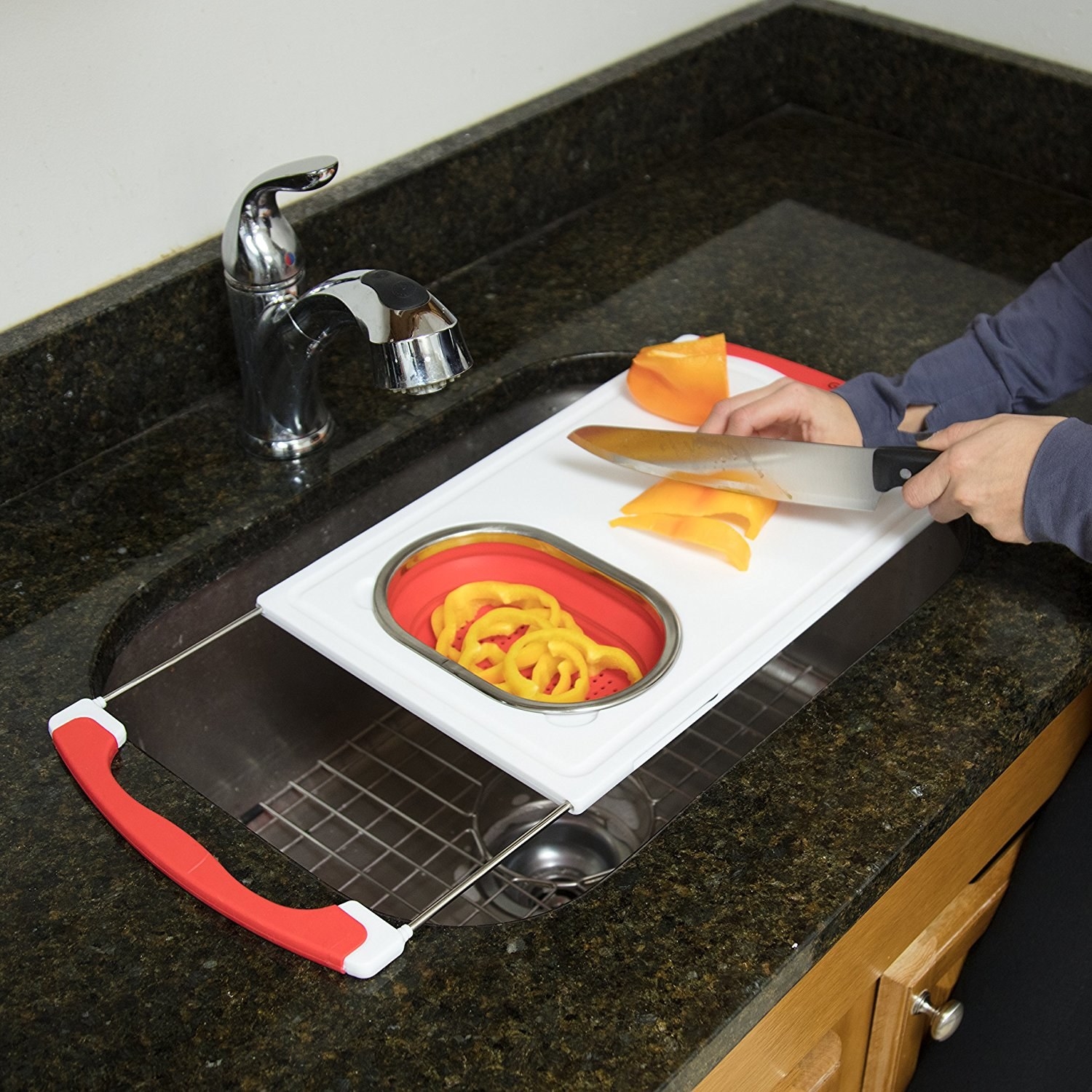 A lifestyle shot of the cutting board, with a draining dish and adjustable handles, being used to cut peppers 