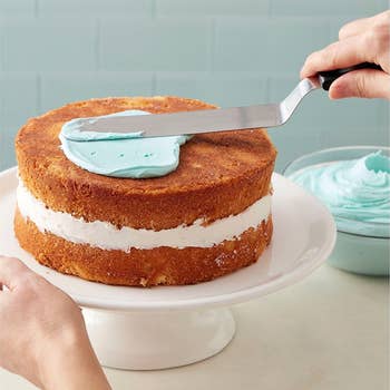 hands using the skinny spatula to frost a cake