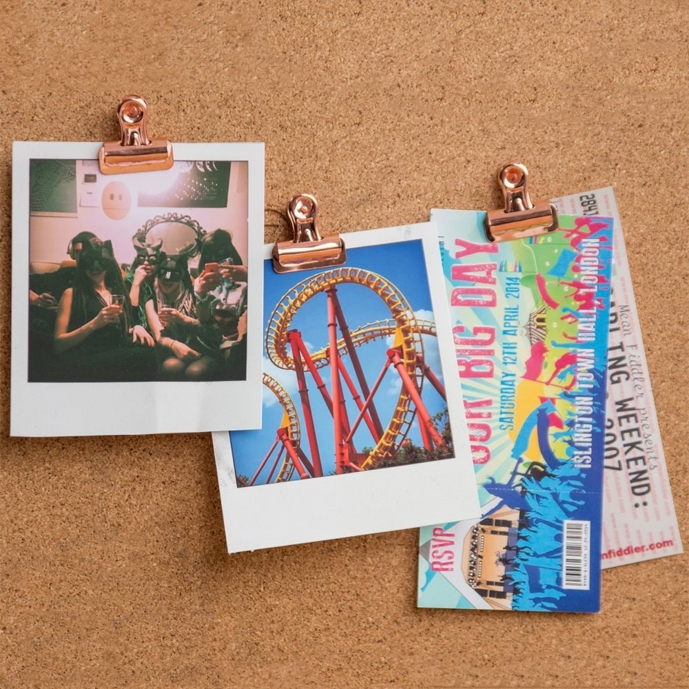 polaroids and concert tickets held up with clips on a corkboard 