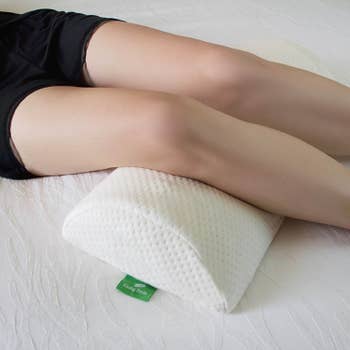 model sleeping with both legs draped over knee pillow