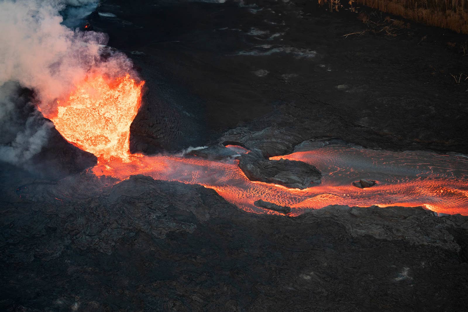 Lava erupts from a fissure, surrounded by a horseshoe-shaped wall of hardened lava.