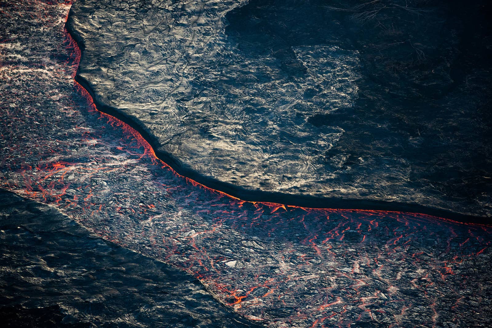 A river of red-hot lava is seen flowing through a channel of hardened lava. At its peak, the lava has moved as fast as 22 mph.