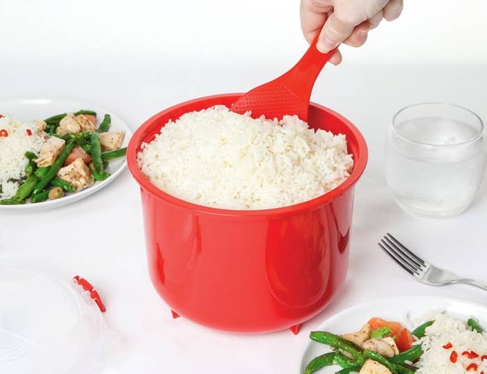 A hand scooping rice out of the red bow/cooker