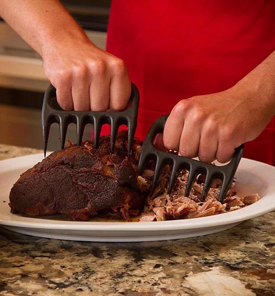 Hands using the metal claw-shaped tools to shred a hunk of meat