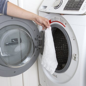 A hand tossing the towel in a washing machine