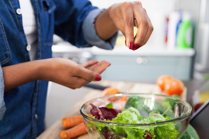 Sprinkling salt on top of a bowl of salad greens.