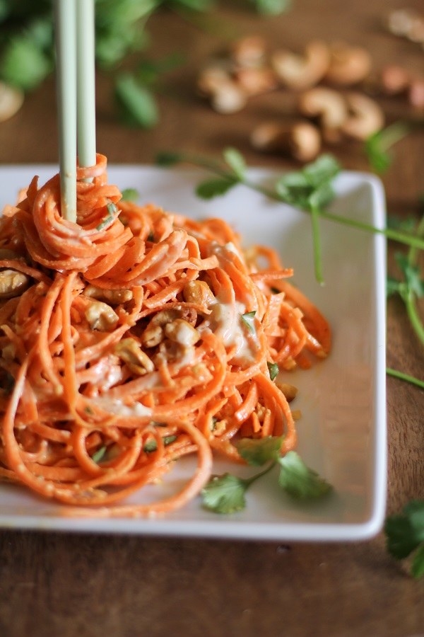 A plate of spiralized carrot noodles topped with chopped nuts and garnished with herbs on a wooden table