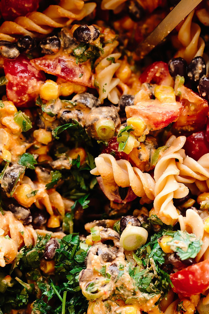Close-up of a vibrant, creamy pasta salad with fusilli, black beans, corn, tomatoes, green onions, and fresh cilantro