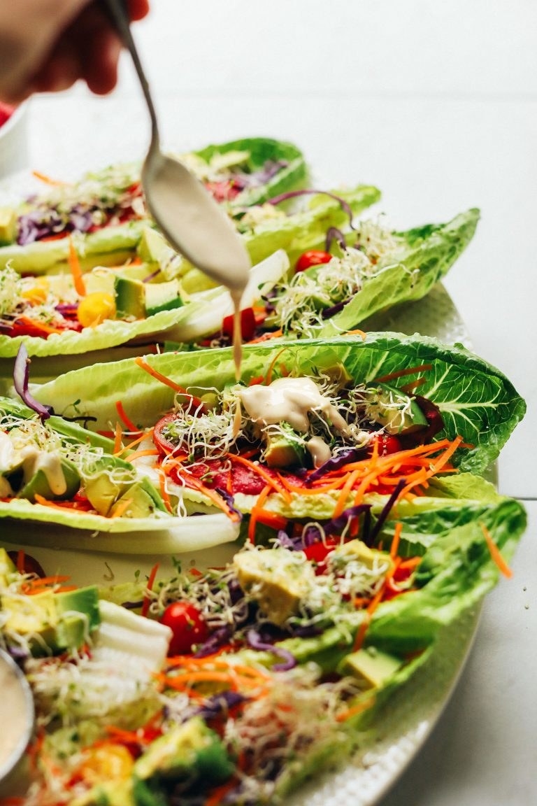romaine lettuce with sprouts, avocados, lettuce, carrots, and more on top of it