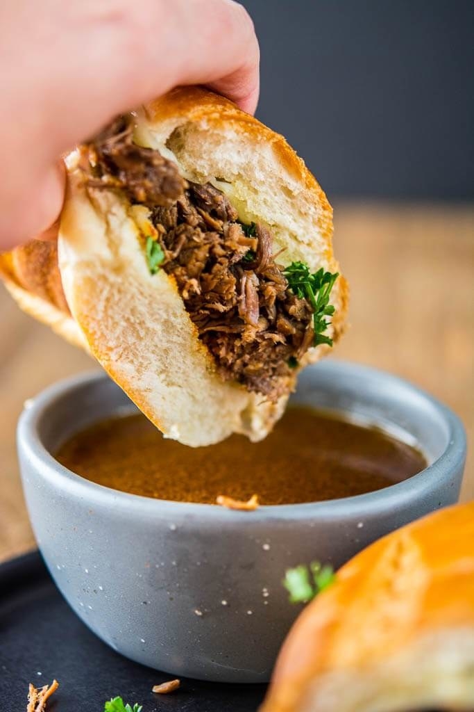 A French Dip sandwich being dunked into a small bowl of au jus