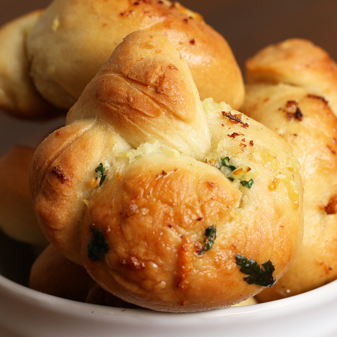 Você vai precisar de:Pão1 ⅔ xícaras de farinha de trigo1 colher de chá de fermento seco instantâneo1 colher de chá de sal1 xícara rasa de água morna2 colheres de chá de azeiteFarinha extra, para polvilharManteiga de alho3 colheres de sopa de manteiga derretida4 dentes de alho amassados1 punhado de salsinha picadaModo de preparo:1. Para o pão, misture a farinha, o fermento e o sal, e faça um furo no meio.2. Despeje a água e 1 colher de chá de azeite no furo e misture.3. Amasse por uns 7-10 minutos, até a massa ficar elástica.4. Unte uma tigela com a outra colher de chá de azeite, coloque a massa na tigela, cubra e deixe crescer em um lugar quente por 1 hora (ou até dobrar de tamanho).5. Preaqueça o forno a 180° C.6. Divida a massa em 9 bolinhas e depois as enrole em tiras longas, dobrando-as para formar um nó.7. Coloque os nós em uma assadeira e leve ao forno por 10 minutos.8. Prepare a manteiga de alho misturando a manteiga, o alho e a salsinha.9. Passe a manteiga nos nós e leve ao forno por mais 5 minutos.10. Bom apetite!