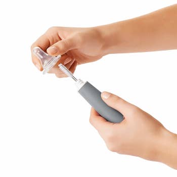 hands cleaning a bottle nipple with the brush