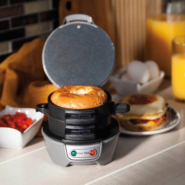 The silver sandwich maker with a bagel slice loaded on the top cooking plate
