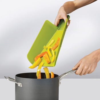 The same cutting board, held over a pot with the two sides folded up to form a funnel for pouring the peppers into a pot