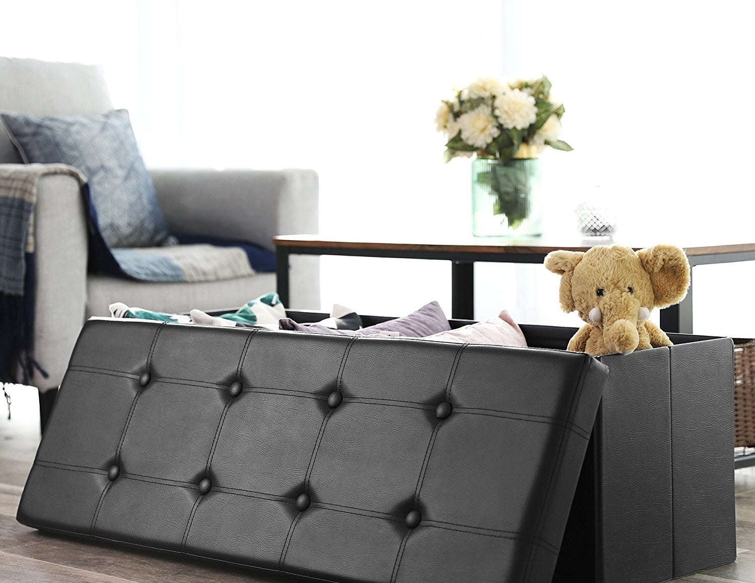 The storage bench in black with the tufted lid on the side of it to show that it is filled with toys and pillows