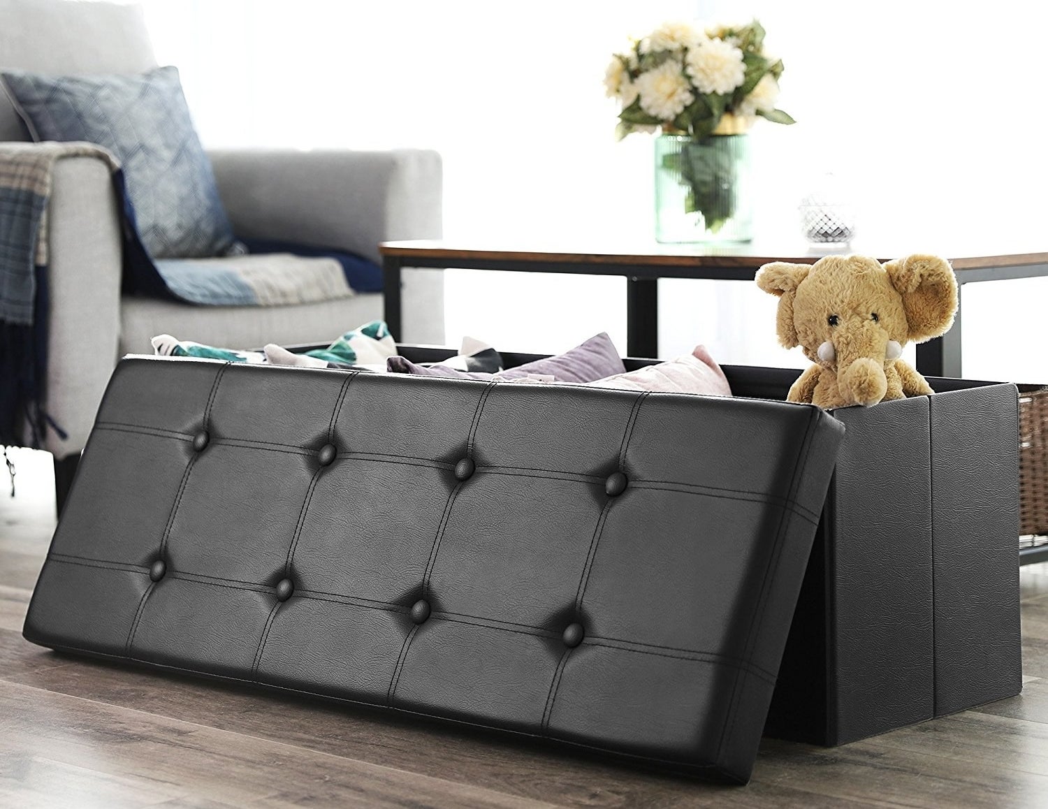 The storage bench in black with the tufted lid on the side of it to show that it is filled with toys and pillows