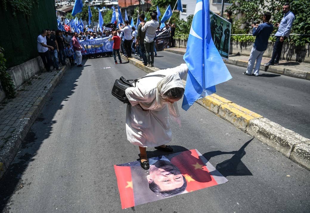 東トルキスタン（ウイグル人の分離主義者が「新疆」に対して用いる名称）の旗を手に持ち、中国の習近平国家主席のポスターに唾を吐きかける女性。7月5日、イスタンブールにある中国領事館の前で行われた抗議運動での一幕。