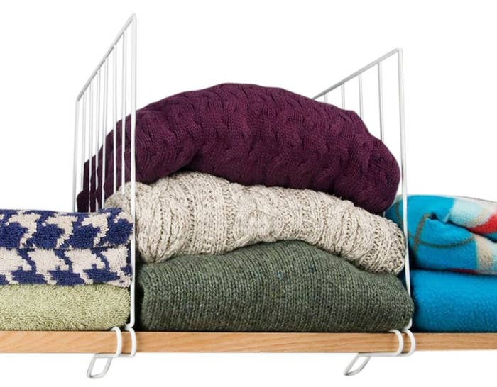 wooden shelf with white wire shelf dividers in between vertical stacks of sweaters and blankets